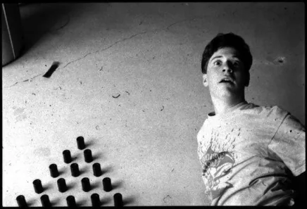 Black and white photograph: a young man lying on a concrete floor beside a neat grid of film canisters